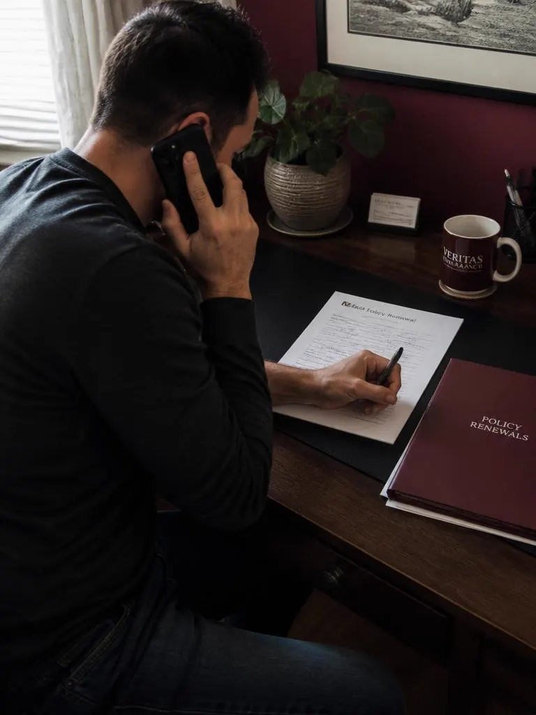 Advisor at a home desk annotating a policy renewal letter during a phone call